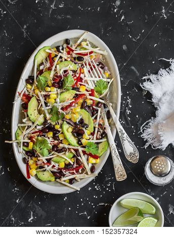 Salad with corn beans avocado and tortilla. Mexican black bean salad. On a dark background top view