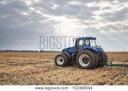 Tractor working in a field, agricultural machinery in the work, tractor in the background cloudy sky