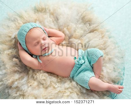 funny newborn boy sleeping with hands behind his head on round fluffy bed