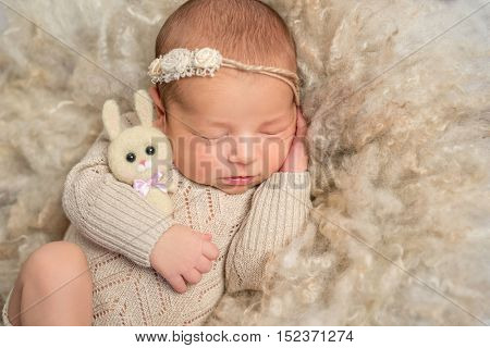 portrait of sweet sleeping newborn girl in jumpsuit with toy hare on fluffy blanket