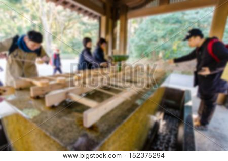 Blurred background . Unidentified people rinse hands and mouth at Temizuya. Temizuya is a Shinto water ablution pavilion for a ceremonial purification rite known as temizu.