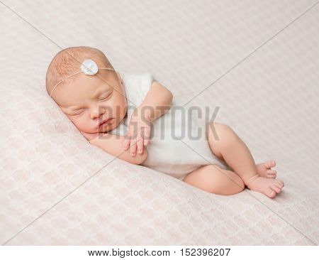 sweet sleeping newborn girl with flower on her headband in white suit