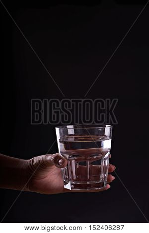Woman holds a glass of water. Give a glass of water. Drink more water. Water for life. Black background.