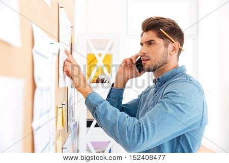 Close up portrait of a young concetrated casual businessman talking on the phone and pointing at board