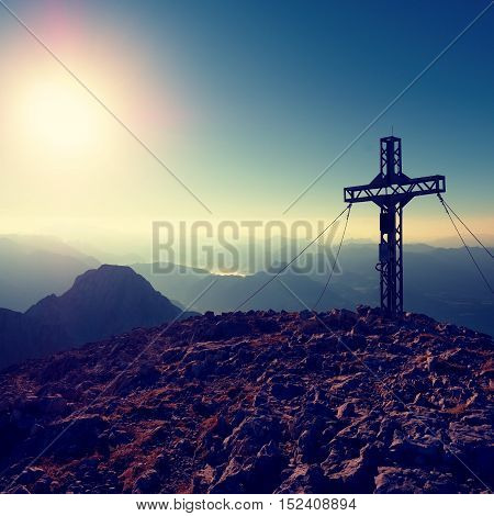 Cross Raised  At Alpine Mountain Peaksharp Rocks, Sun In Sky.