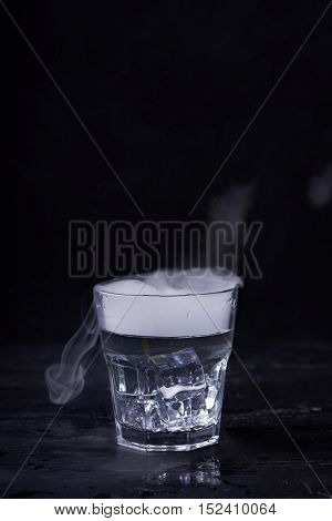 Hot water with a lot of steam in a glass at a black background. Dark photo. Concept photo: three state of water - ice, water, steam.