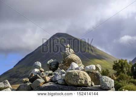 Focus on a small stone cairn of carefully balanced rocks in front of the beautiful landscape of Isle of Skye Scotland and the conical shape of Glamaig in the Red Hills mountain range.
