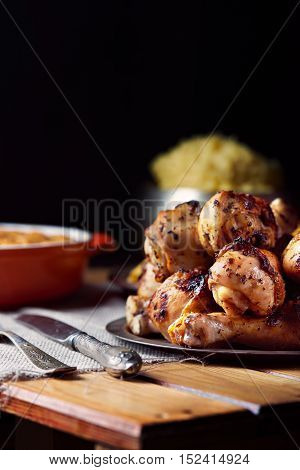 Close view of grilled chicken legs, knife, and fork mash potatoes on a table on a black background. Dark photo. Vertical shot