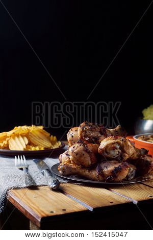 Close view of grilled chicken legs, knife, and fork mash potatoes, chips on a table. Dark photo. Vertical shot