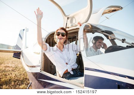 Young beautiful woman in sunglasses waving from the plane cabin after landing