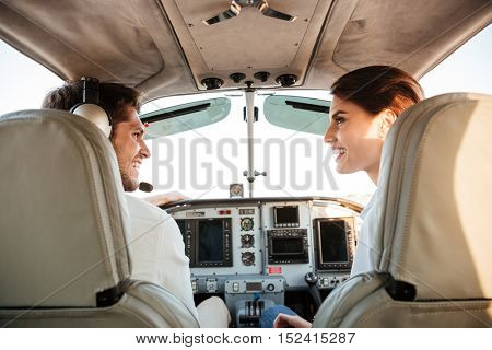 Beautiful young couple looking at each other and laughing while sitting inside airplane cabin