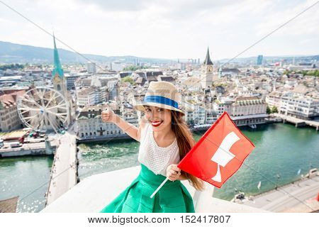 Young female tourist with swiss flag on the top of the tower in Zurich city. Woman having a great vacation in Switzerland