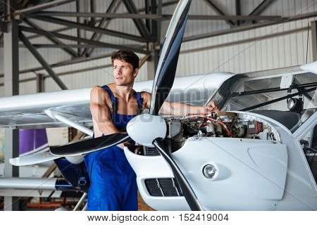 Handsome young repair man fixing plane engine at angar