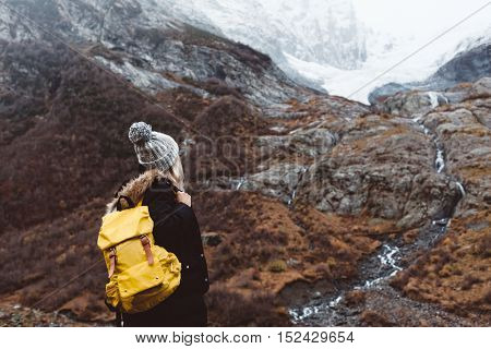 Young woman with backpack trekking in mountains. Cold weather, snow on hills. Winter hiking.