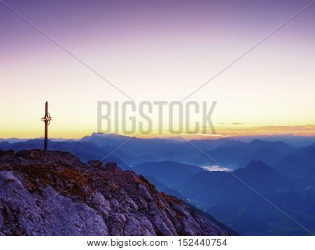 Steel Crucifix At Mountain Peak In Alps. Sharp Rocky Summit, Daybreak Sun In Sky.
