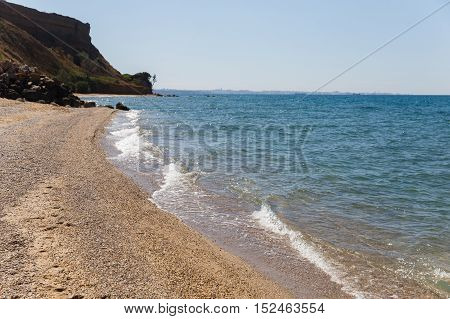 Wild beach with small pebbles and large rock formations. Clean sea soft washes coastline