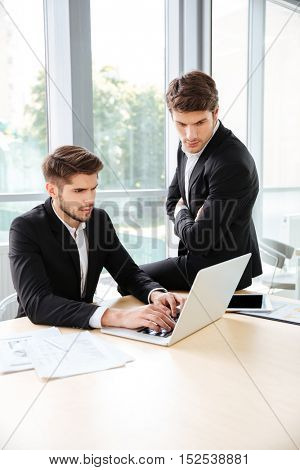 Two concetrated young businessmen using laptop in office together