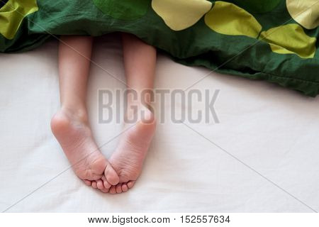 Child laying in bed with bare feet out