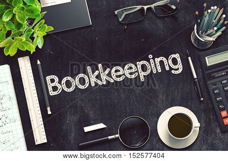 Bookkeeping Handwritten on Black Chalkboard. Top View of Black Office Desk with a Lot of Business and Office Supplies on It. 3d Rendering. Toned Illustration.