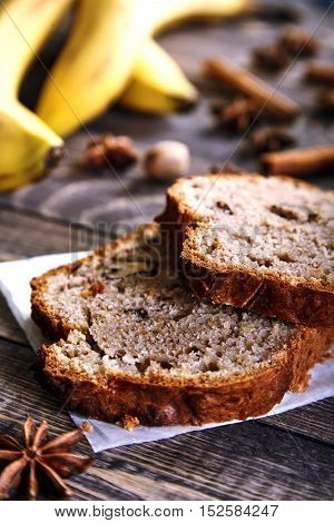 Delicious slices of homemade banana bread with nuts. Fragrant dessert for cup of tea on wooden table. Fresh bananas, cinnamon sticks, stars of anise and walnuts in the shell next to it. Banana loaf