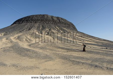 Egypt Black Desert, view of the mountain backdrop, photographer girl near the impressive mountain covered with crystals. Black education are of volcanic origin. A popular place for tourists