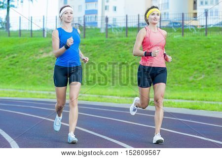 Concepts of Jogging and Healthy Lifestyle. Two Young Caucasian Girlfriends in Athletic Sportswear Having Jogging Exercises Around the Sport Venue. Horizontal Image