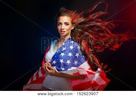 Young attractive girl wrapped in a US flag. She a T-shirt and shorts with a print of the flag. Long curly hair flying. Portrait of a real patriot. Stars and Stripes.