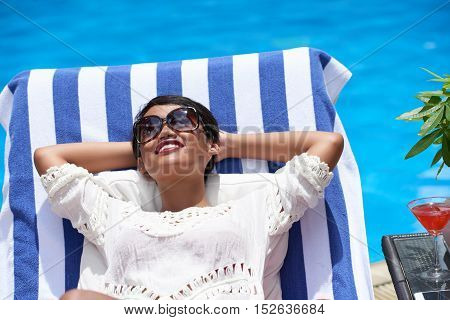 Asian smling young woman enjoying sunbathing by pool