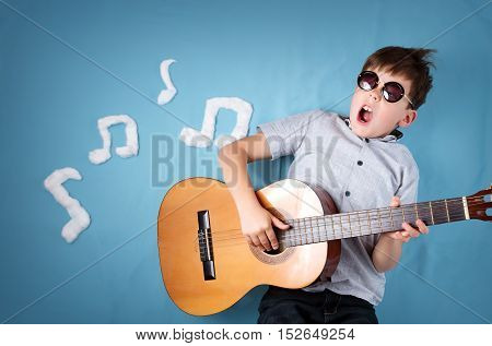 happy seven years old boy on blue blanket background with acoustic guitar and musical notes. Young guitarist singing song
