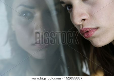Portrait of an attractive caucasian woman whose face is mirrored on a glass like reflective surface of a tv screen