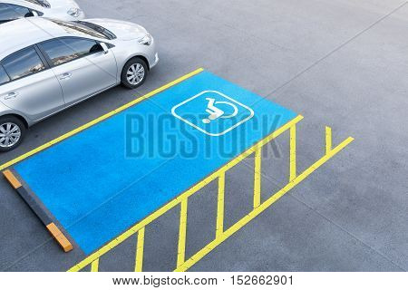International handicapped symbol painted in bright blue on a shopping center parking space. The space is clearly marked on either side with additional white diagonal stripes.