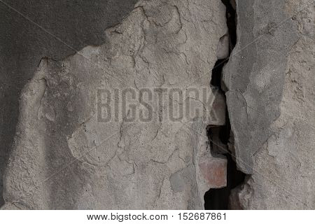 Gray obsolete plastered wall divided by wide split. Rough uneven texture