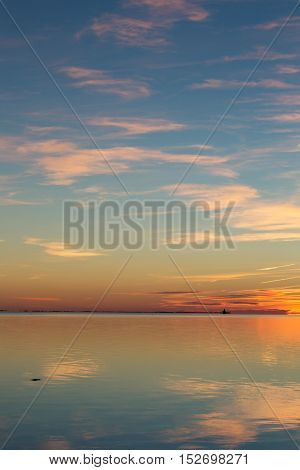 Reflections of a sunset in still ocean water.