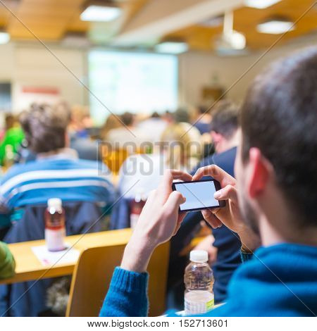 Workshop at university. Rear view of participant listening to lecture and making notes on smarth phone. Using online tools and aplications in education and everyday life.