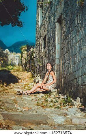 Feminine portrait of young romantic woman sitting on oldest stone road in Old Bar, Montenegro. Summer travelling, European vacation, travel concept. The ancient fortress and ruins in Stari Bar in Crna Gora.