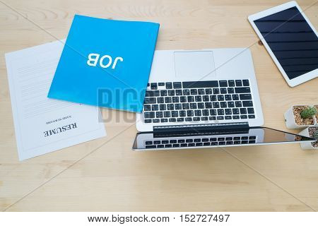 wood table with laptop tablet cactus flower on pot and resume information. job search concept. office desk with office equipments and resume information. view from top above table.