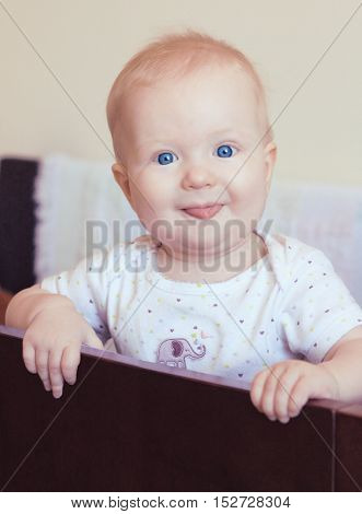 Cute funny baby girl standing in her crib smiling and showing her tongue.