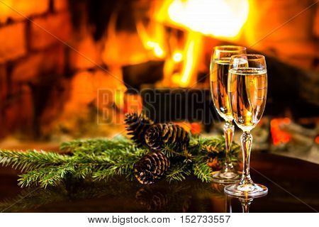 Two glasses of sparkling white wine and New Year Christmas decoration in front of warm fireplace. Romantic, cozy relaxed magical atmosphere near fire. New Year or Christmas concept