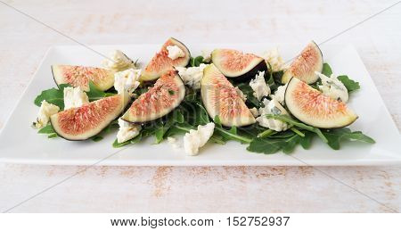 Fig arugula blue cheese salad on white plate on wooden table selective focus