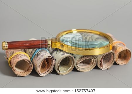 Rolls of Indian Currency Rupee Notes with magnifying glass on gray