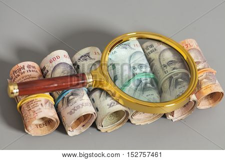 Rolls of Indian Currency Rupee Notes with magnifying glass on gray