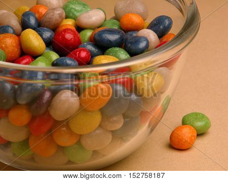 Different sweets in vase. Small size of colorful candy, yellow, green, white, brown, in glass, small glass, clear glaze, on the table, yellow background