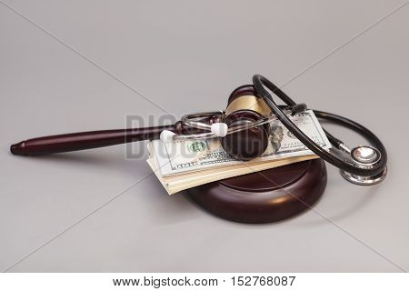 Stethoscope with judge gavel and dollar banknotes on gray background