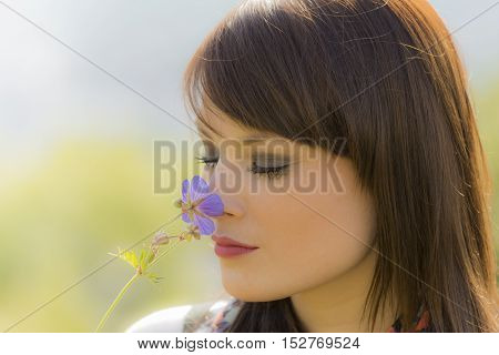 Beautiful meditative girl sniffing a flower. The young woman is enjoying the natural beauty. Wonderful picture with nice colors.