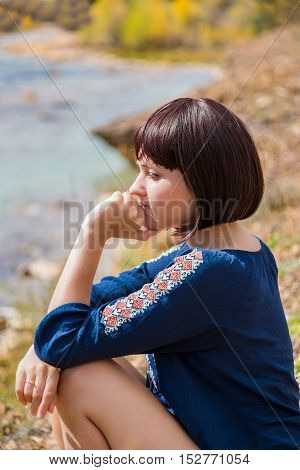 Young woman sitting contemplating by light green creek during autumn with hand on face