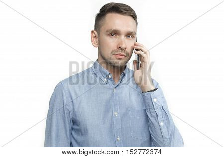 Serious young man in blue shirt talking on mobile isolated on white background