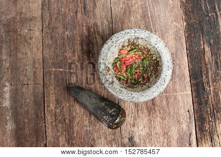 chilli pepper in stone mortar on the wooden table paste spicy herb ingredient food Thailand ancient style. Image Top view
