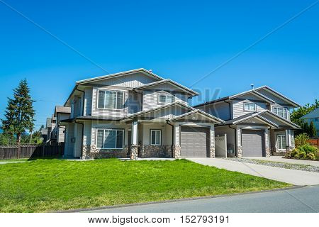Residential duplex building with concrete drive ways and green lawns in front. Two family dwelling with asphalt road in front