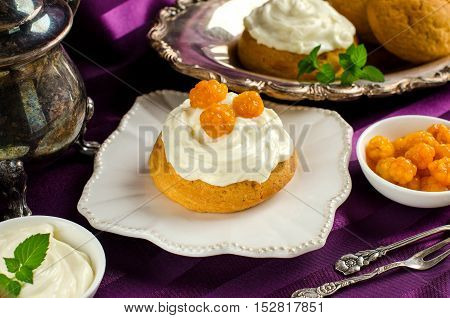 Cream cakes. Yellow cloudberries. Mint leaves. The desserts on the plate. Cloudberries and cream in bowls. Dessert fork and spoon. Purple background. Silverware.