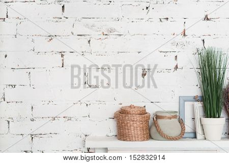 White on white. Wooden white shelf decorated with flowerpots and picture frames against brick wall.